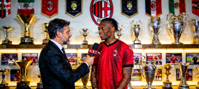 记者正在采访AC米兰球员，背景是俱乐部的荣誉墙